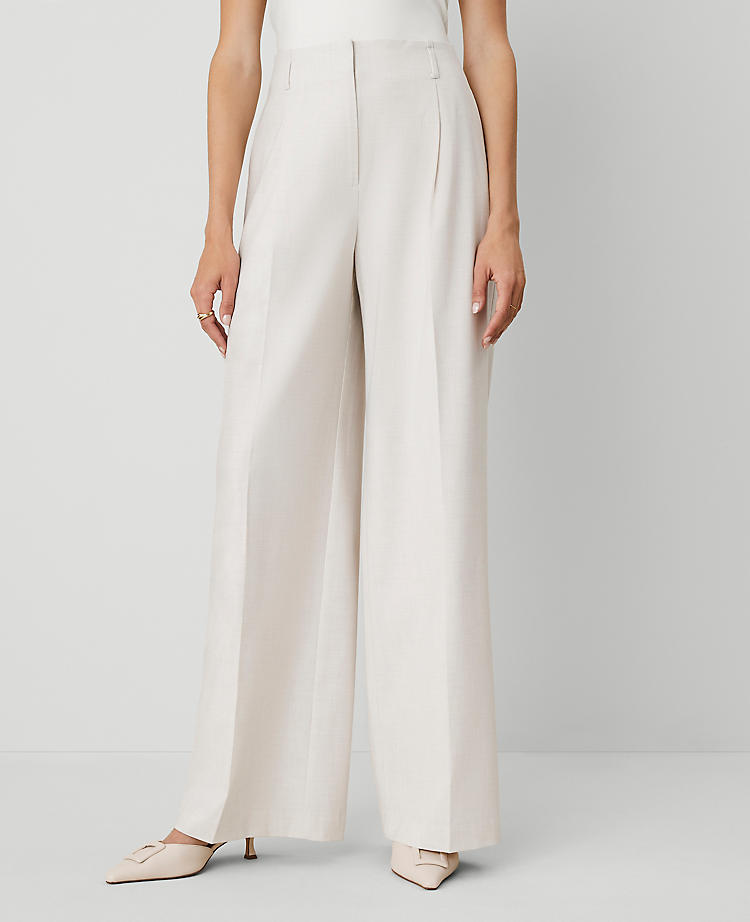 A woman wearing white wide-leg pants with a high waist, front pleats, belt loops, and pockets, paired with beige heels.