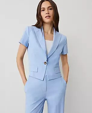 A woman wearing a light blue short-sleeve blazer with notched lapels and a single button closure, styled with matching trousers.