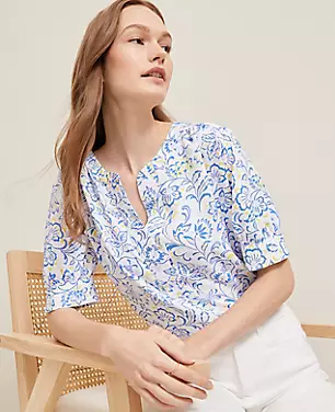 A woman wearing a petite paisley floral blouse with a split neck, shirred shoulders, and elbow-length sleeves.