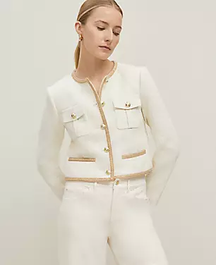 A petite women's white tweed jacket with gold buttons, chest flap pockets, front welt pockets, and a round neckline, shown on a model.