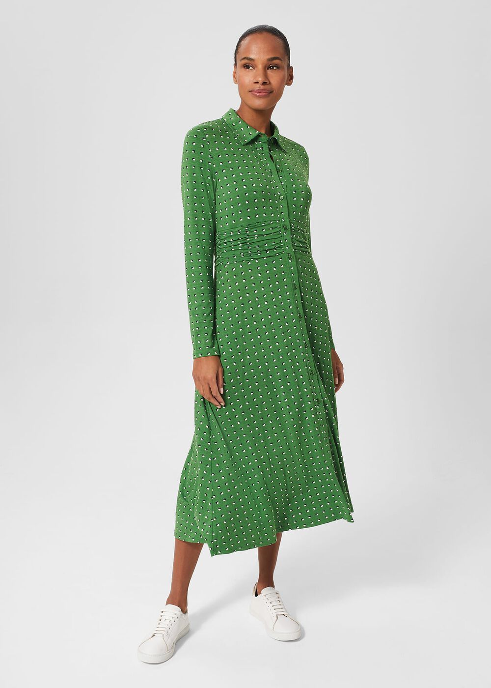 A woman wearing a green, long-sleeved, button-down dress with a micro geometric pattern and a ruched waist, paired with white sneakers.