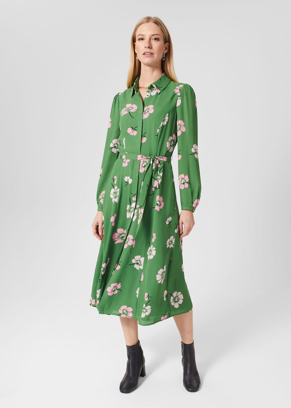 A woman wearing a green floral midi dress with pink and white flowers, long sleeves, and a collar, styled with black ankle boots.