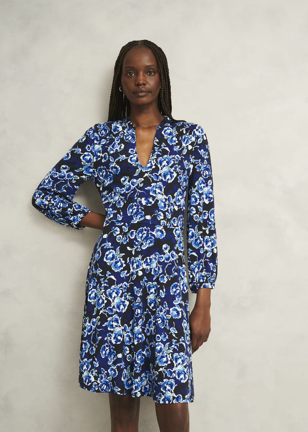 A woman wearing a blue floral dress with a V neckline, blouson sleeves, and a knee-length hem.