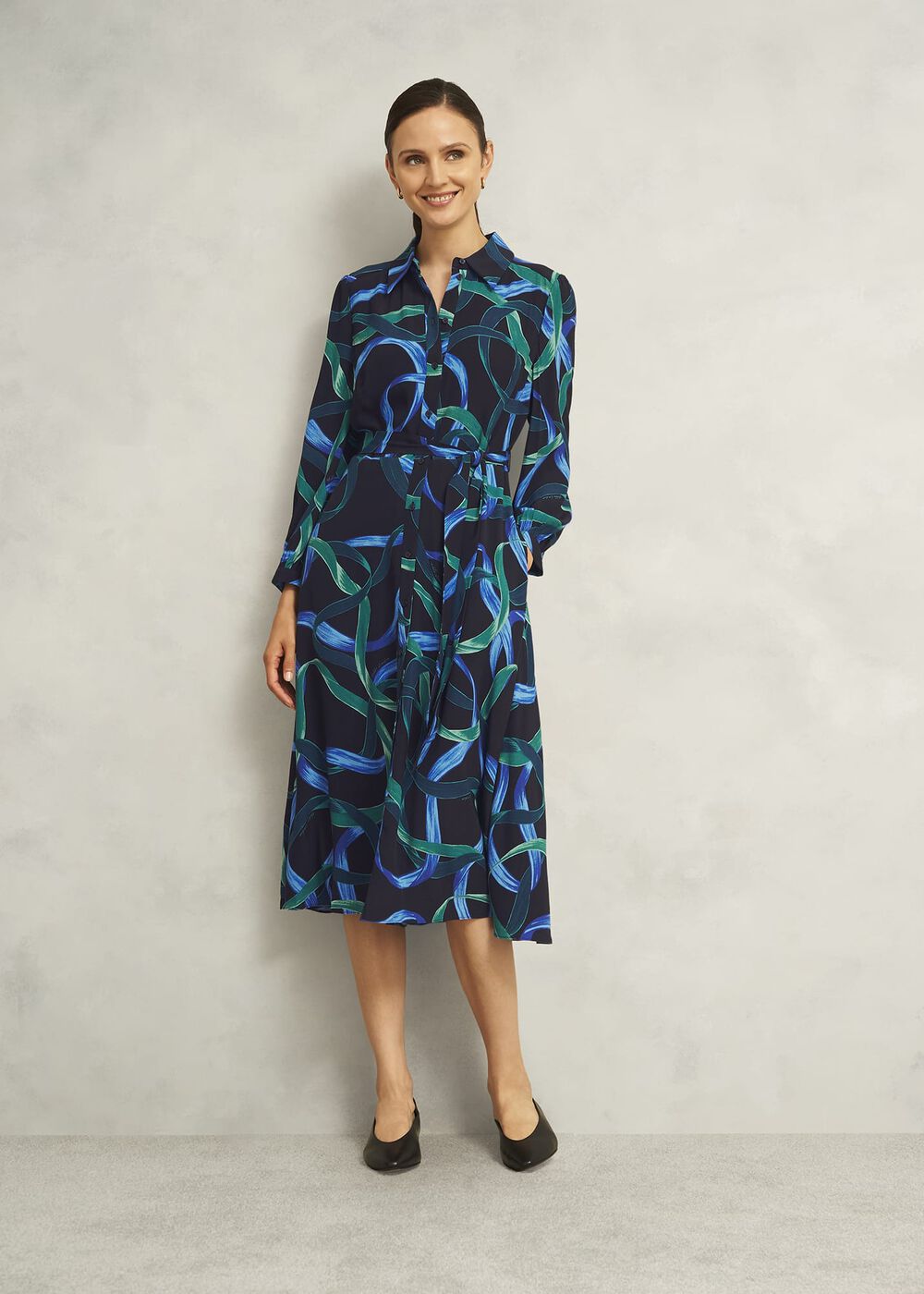 A woman wearing a sleeveless, fitted dress with a collar and front fastening, featuring a blue and green abstract pattern on a navy background.