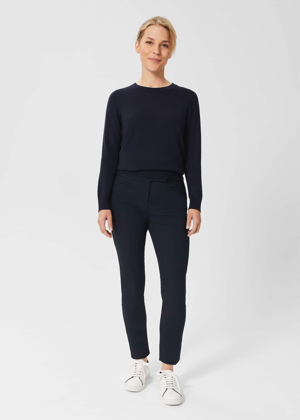 A woman wearing navy blue slim trousers with stretch, paired with a navy sweater and white sneakers.