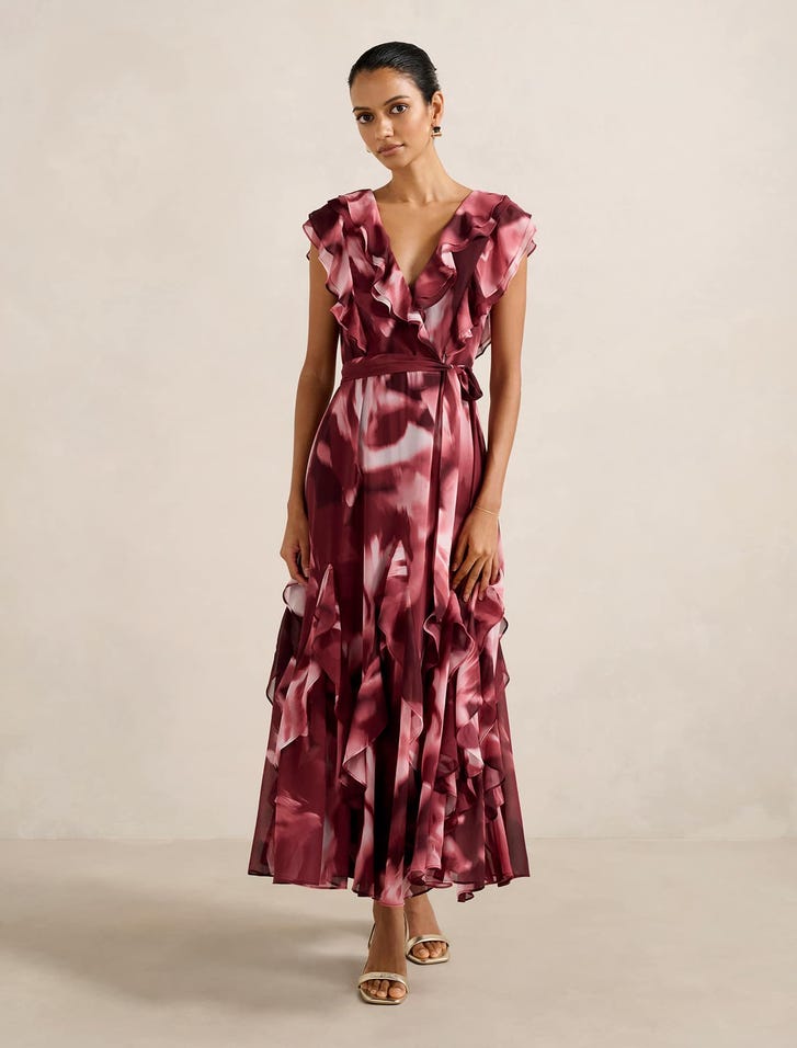 A woman wearing a pink and burgundy floral print midi dress with ruffle details, V-neckline, and waist tie.