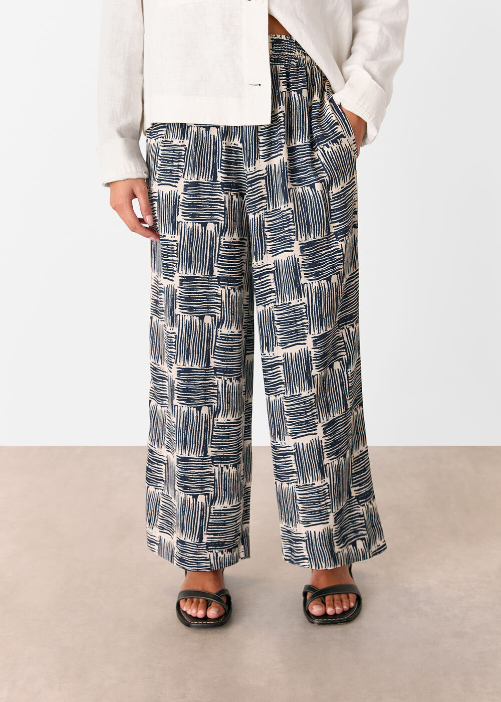 A pair of navy cropped trousers with hatch square pattern, worn with a white top and black sandals.