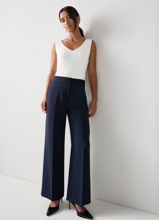 A woman wearing navy wide-leg trousers with a sleeveless white top, standing against a plain white background.