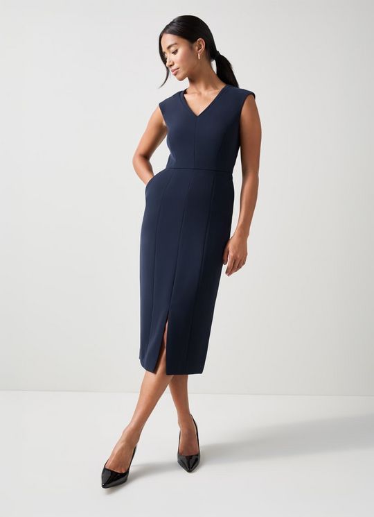 A woman wearing a navy blue sleeveless V-neck shift dress with a fitted silhouette, midi length, and front slit, paired with black heels.