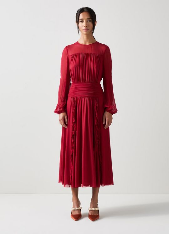 A woman wearing a vibrant red crinkle mesh viscose dress with long sleeves, a crew neckline, and a flowing midi-length skirt with pleats.