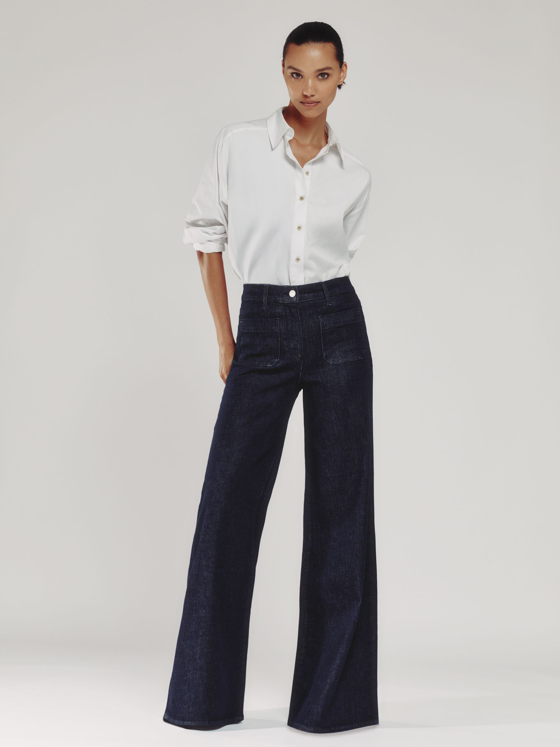 A woman wearing dark blue wide-leg jeans with a high waist, front patch pockets, and a white shirt.