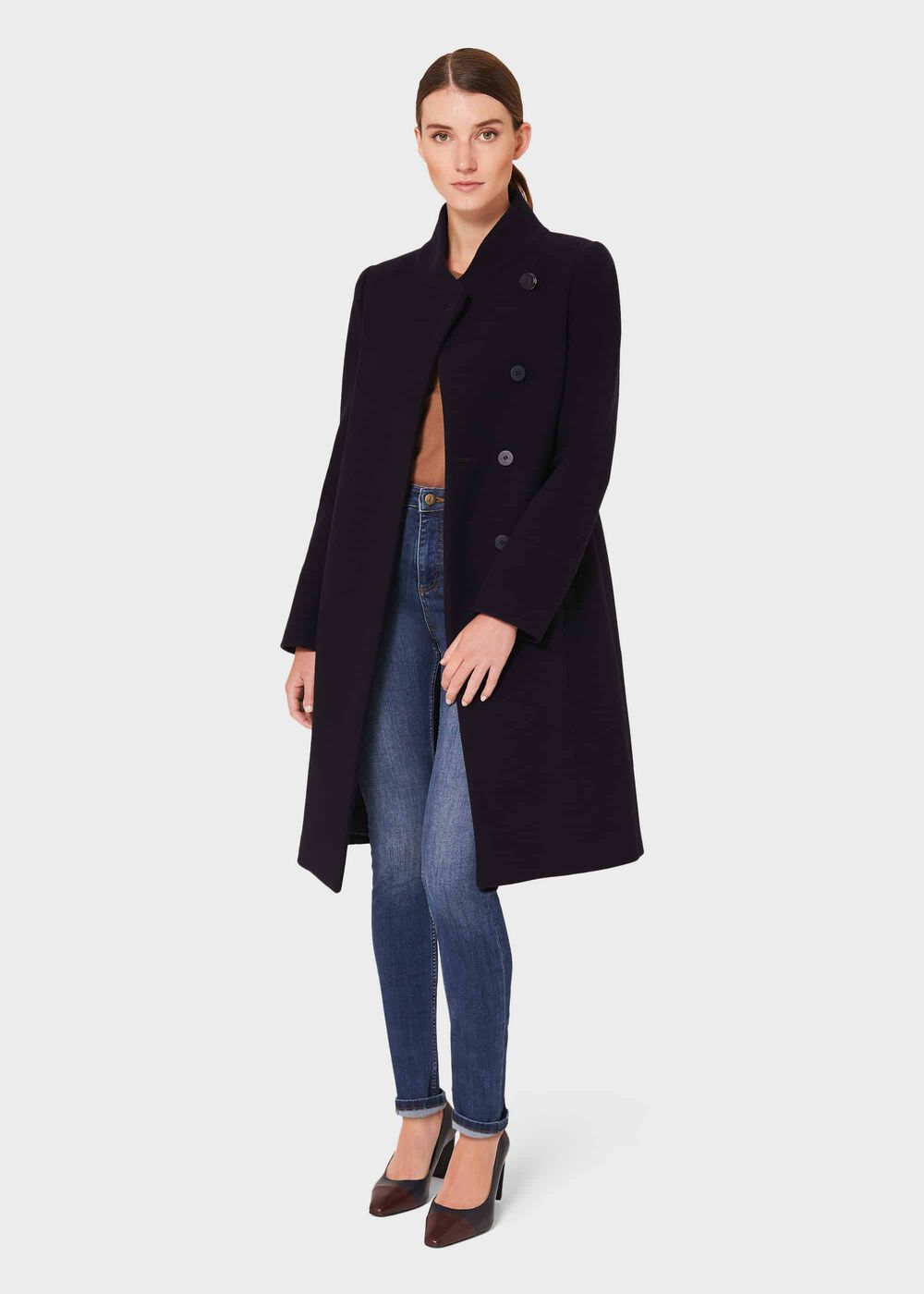 A woman wearing a black wool blend coat with a funnel neck, button fastening, and tailored fit, paired with blue jeans and high heels.