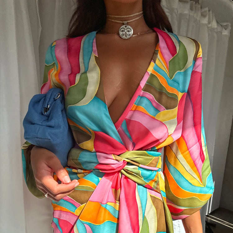 A woman wearing a colorful, abstract print mini wrap dress with a deep V-neckline and long sleeves, tied at the waist.