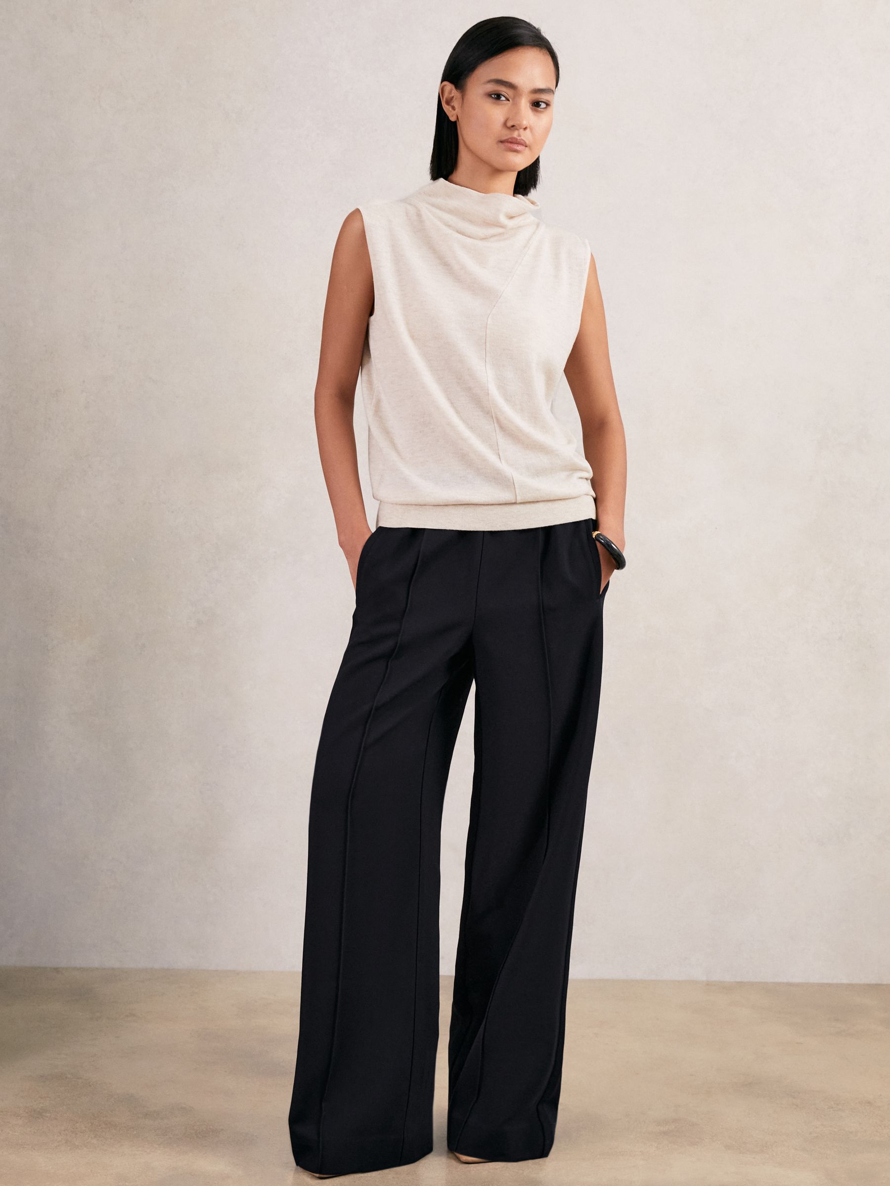 A woman wearing navy wide-leg trousers with an elastic waistband, front pintucks, and pockets, paired with a sleeveless beige top.