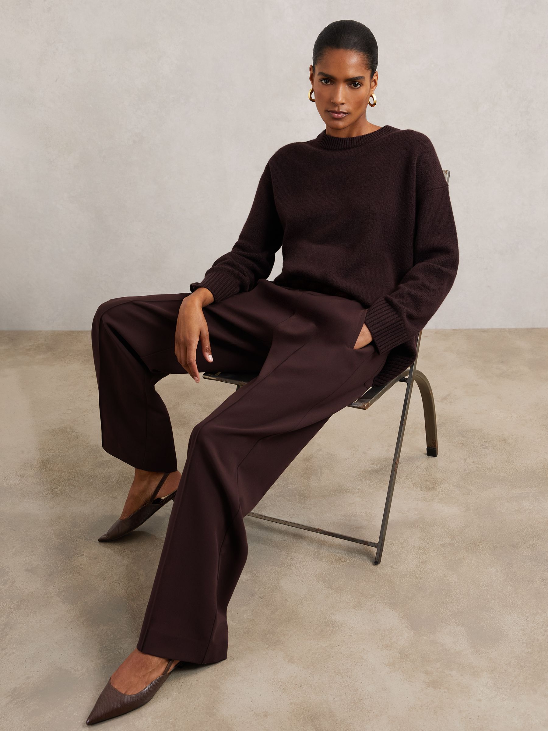 A woman wearing burgundy wide-leg trousers with an elasticated waistband, front pintucks, and pockets, paired with a matching burgundy sweater.
