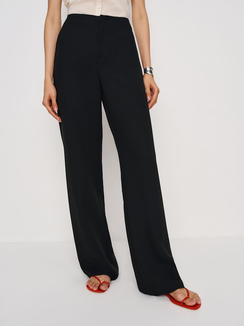 A woman wearing black high-rise pants with a fitted waist and straight leg, paired with a beige top and red sandals.