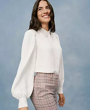 A woman wearing a white blouse with lace collar and blouson sleeves, paired with plaid pants.