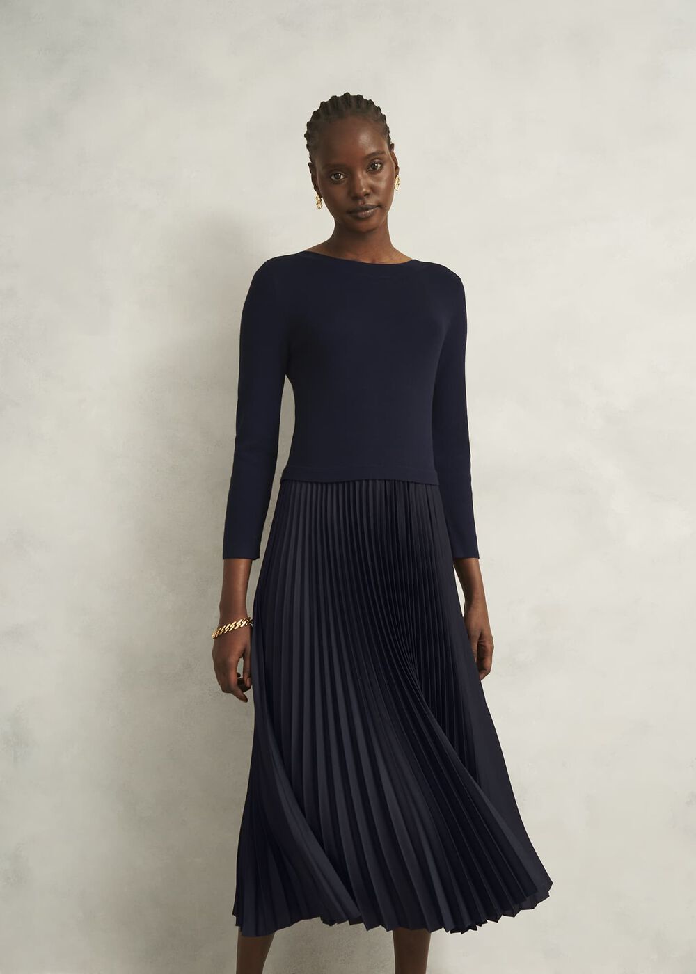 A woman wearing a navy blue dress with a knitted top and a satin pleated skirt, long sleeves, and a boat neckline.