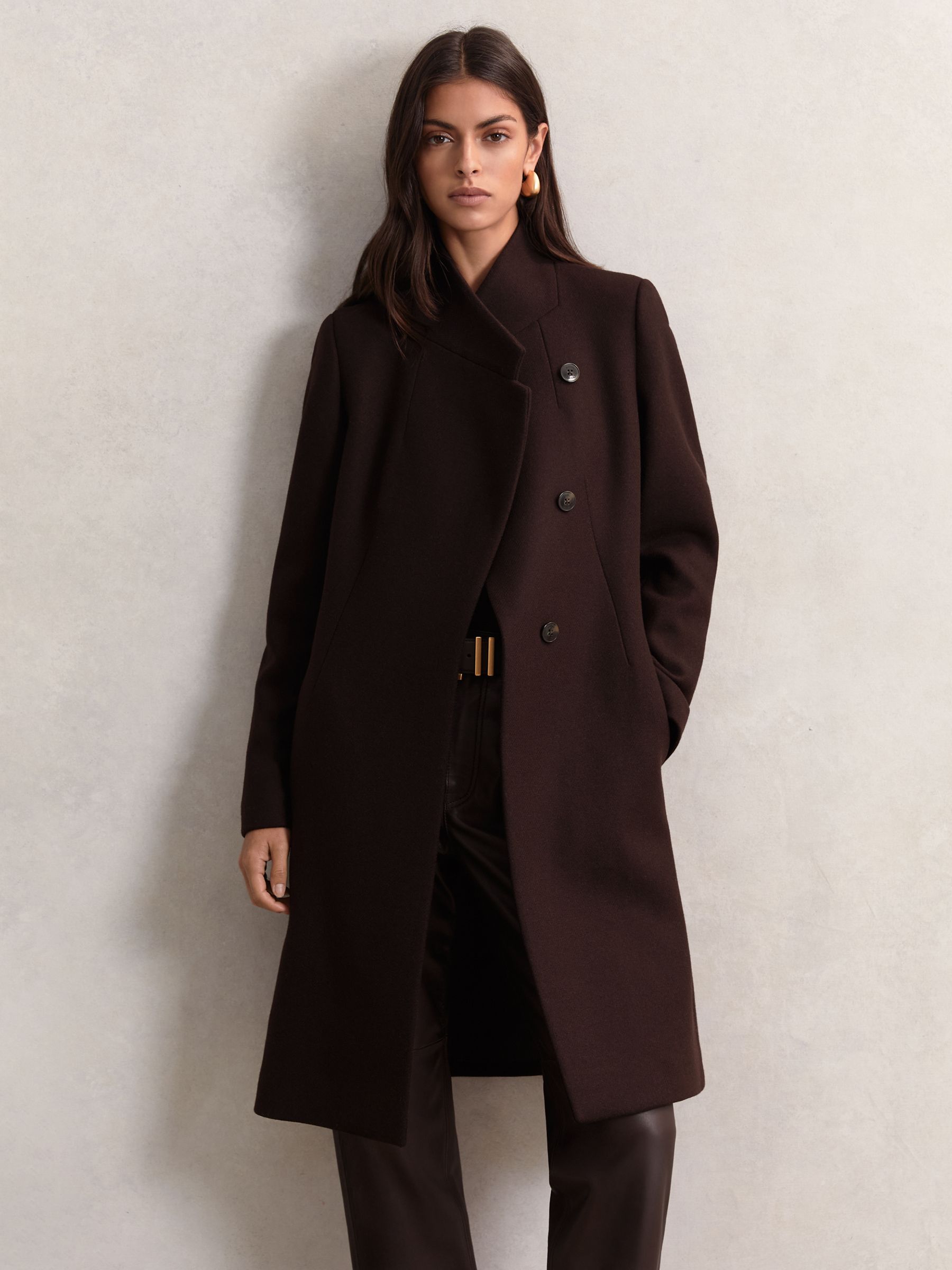 A woman wearing a chocolate brown wool-blend wrapover mid-length coat with a standing collar and concealed buttons.