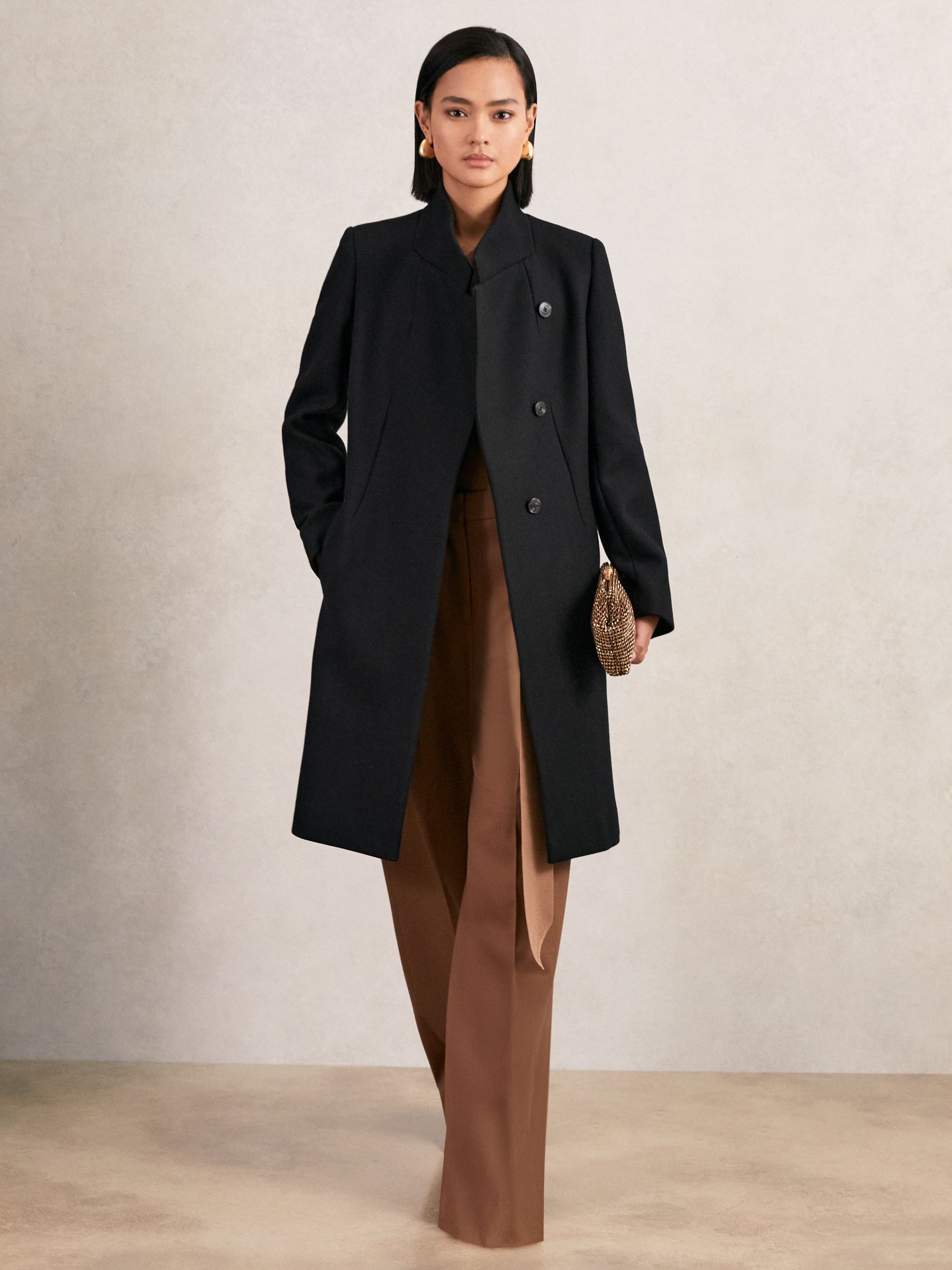 A woman wearing a black wool-blend wrapover mid-length coat with a standing collar and concealed buttons.
