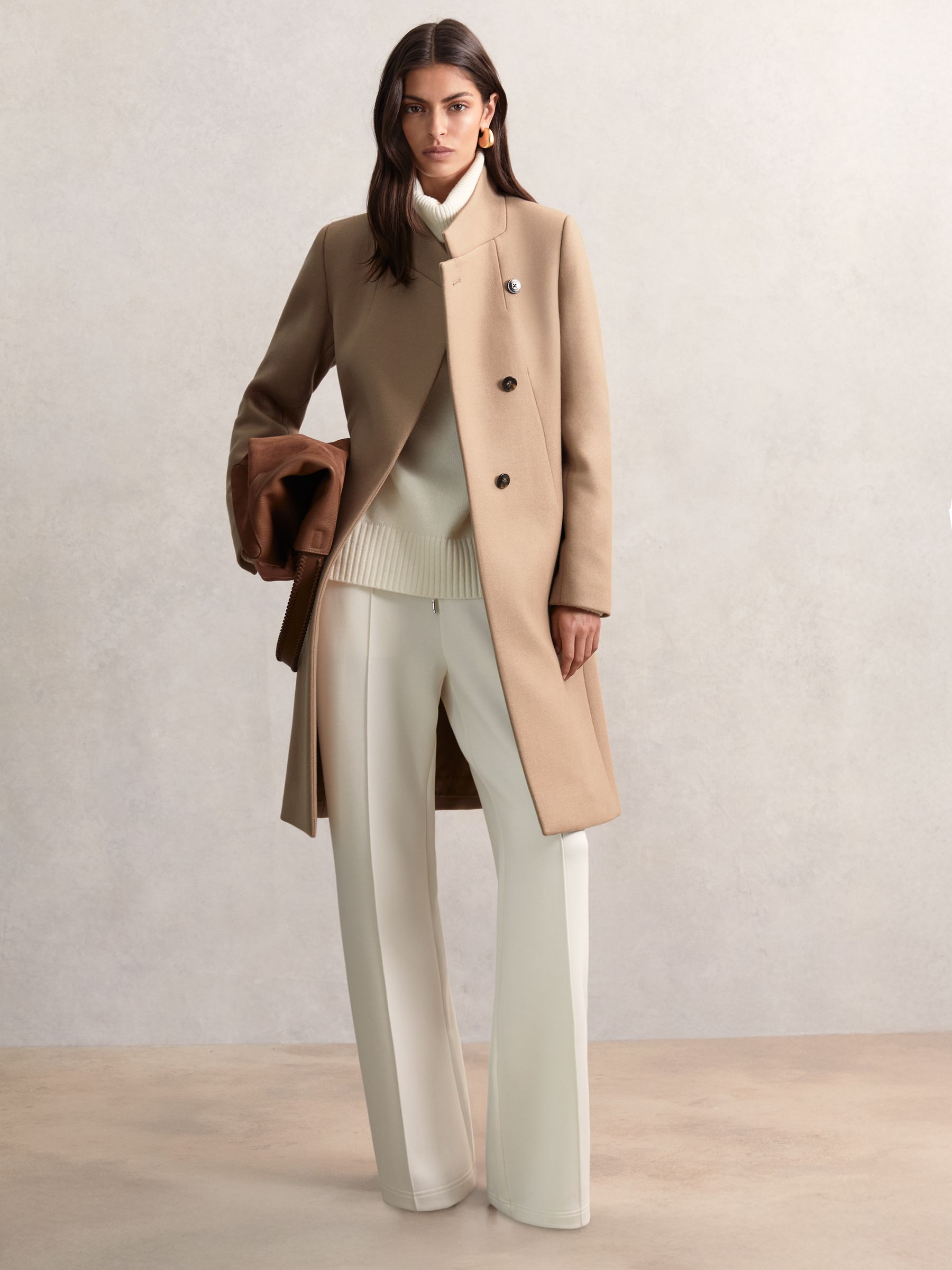A woman wearing a camel-colored wool-blend wrapover mid-length coat with a standing collar and concealed buttons.