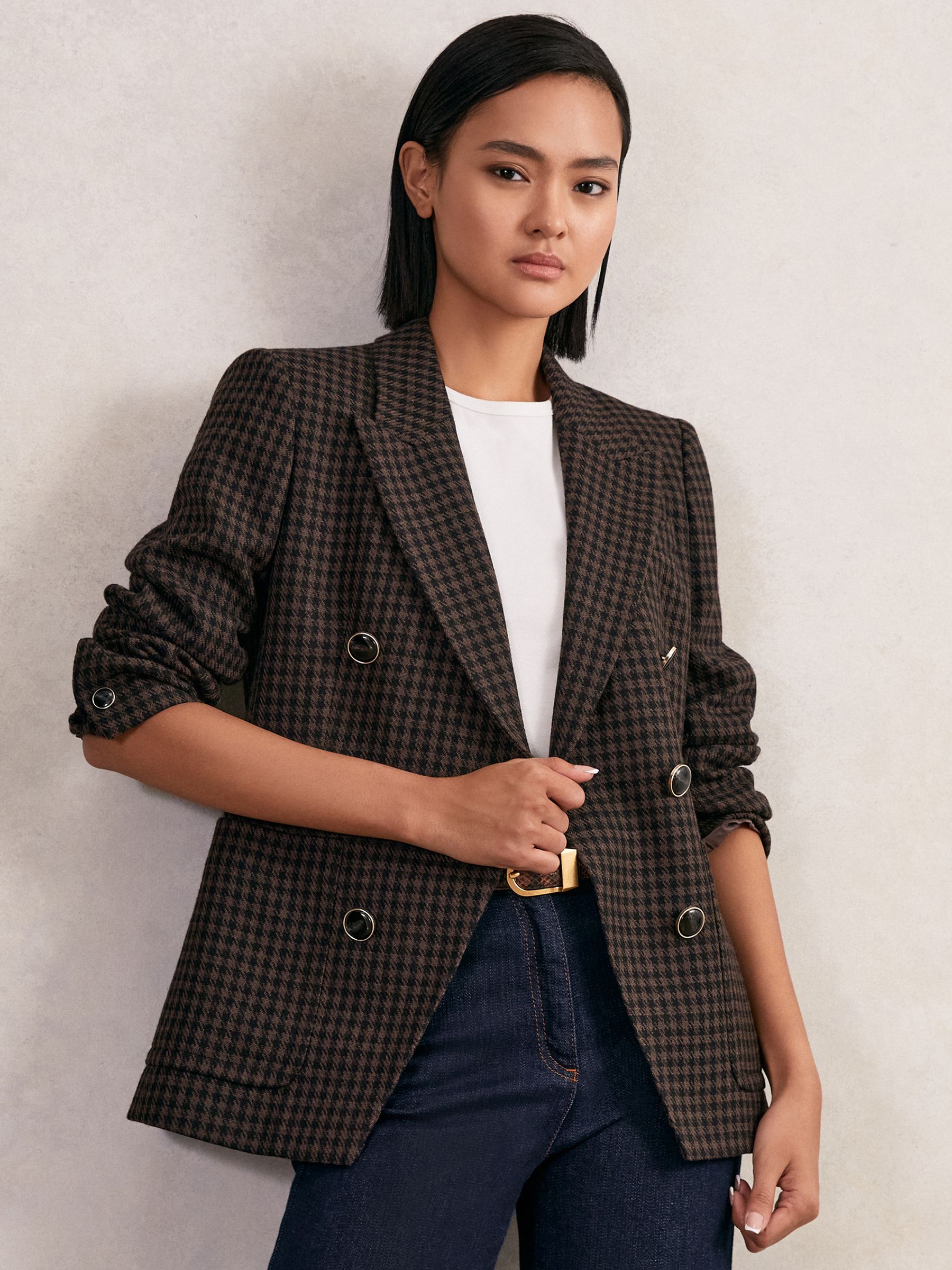 A woman wearing a brown check blazer with peak lapels, double-breasted style, and marbled buttons.