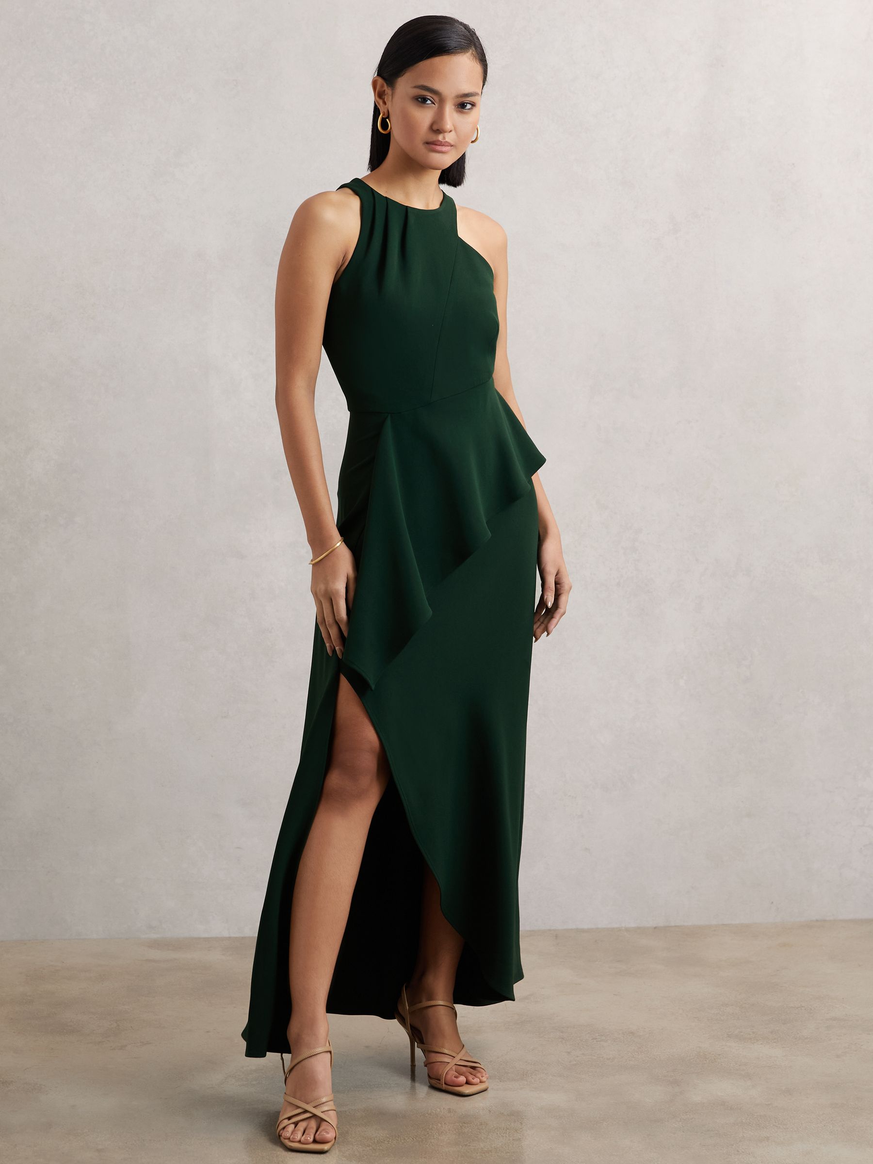 A woman wearing a green sleeveless maxi dress with a racer-style top, gathered neckline, cascading ruffle, and a slashed hemline.