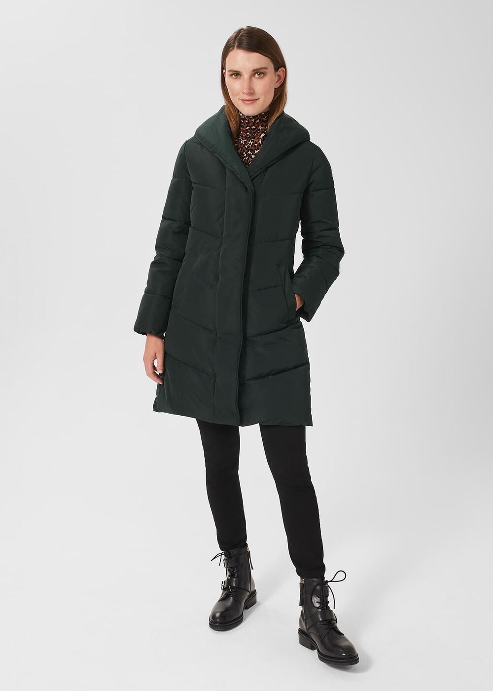 A woman wearing a black, long, lightweight puffer jacket with a shawl collar, chevron padded panels, ribbed cuffs, and fleece-lined pockets.