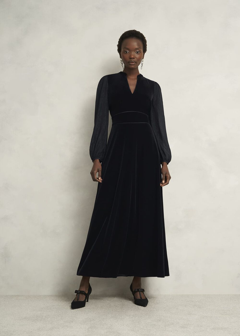A woman wearing a black velvet dress with long semi-sheer sleeves, a V-neckline, and a tie detail at the waist.