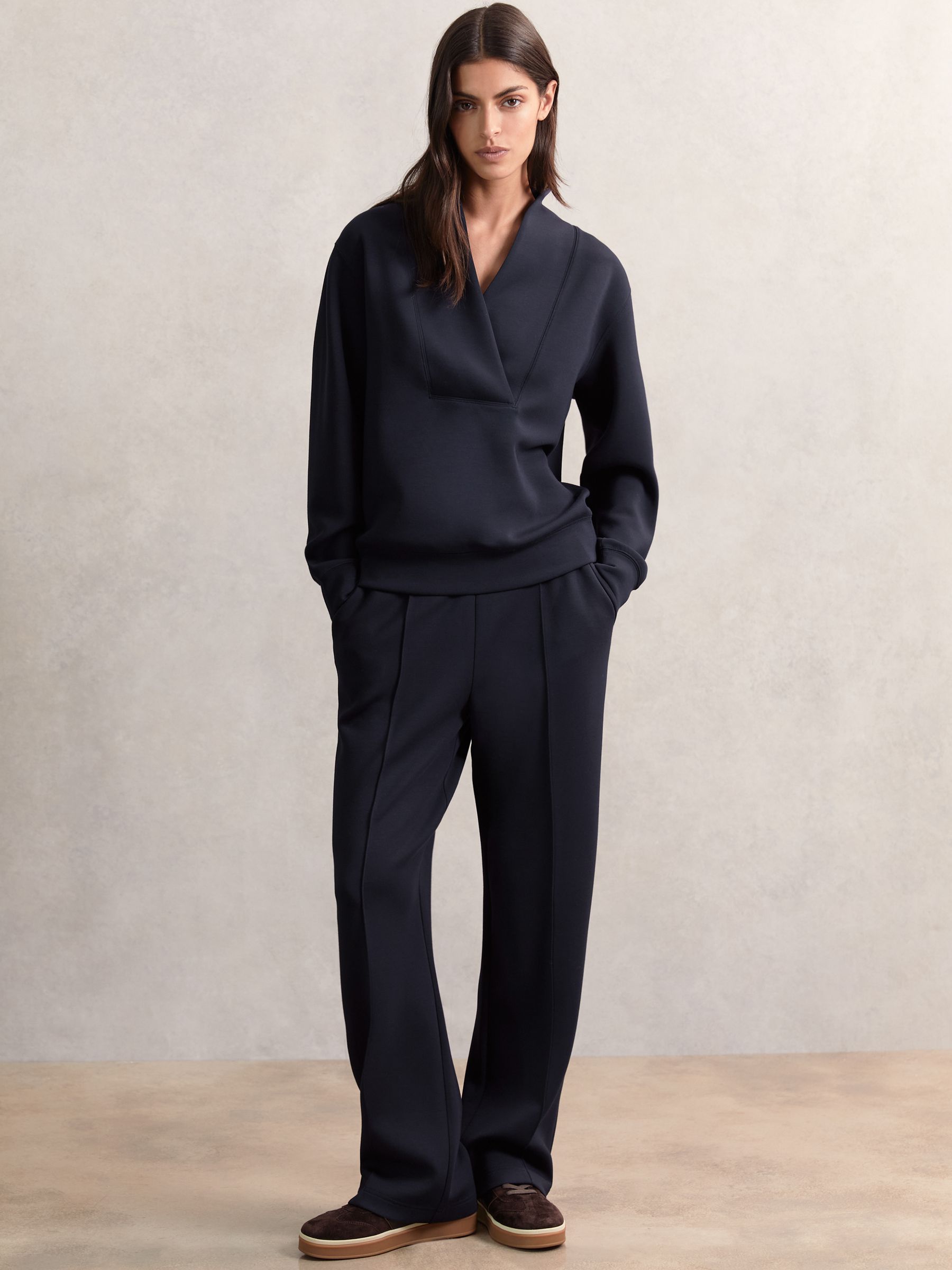 A pair of navy wide-leg joggers with front pintucks, side slip pockets, and an elasticated drawstring waist, made from smooth modal-blend fabric.