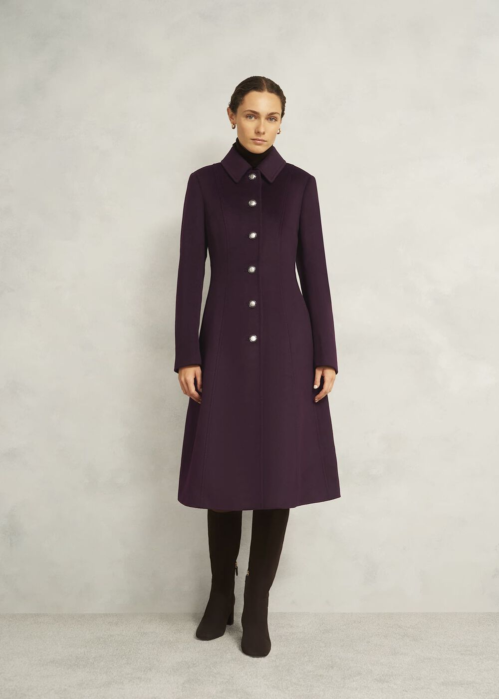 A woman wearing a long, purple wool coat with a button-up front, collar, and fitted waist, paired with black boots.