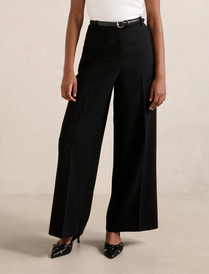 A woman wearing high-waisted black wide-leg trousers with a belt, side pockets, and a white top.