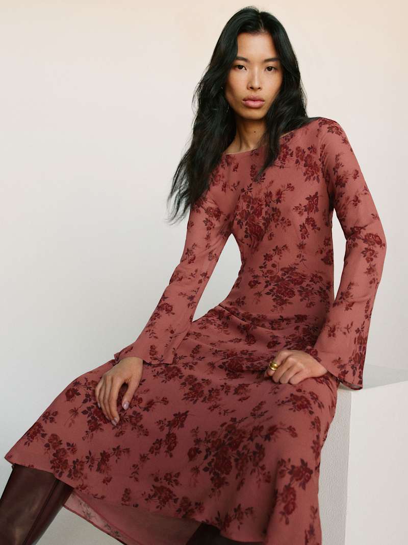A woman wearing a dusty rose long dress with a floral pattern, boat neckline, and long sleeves.