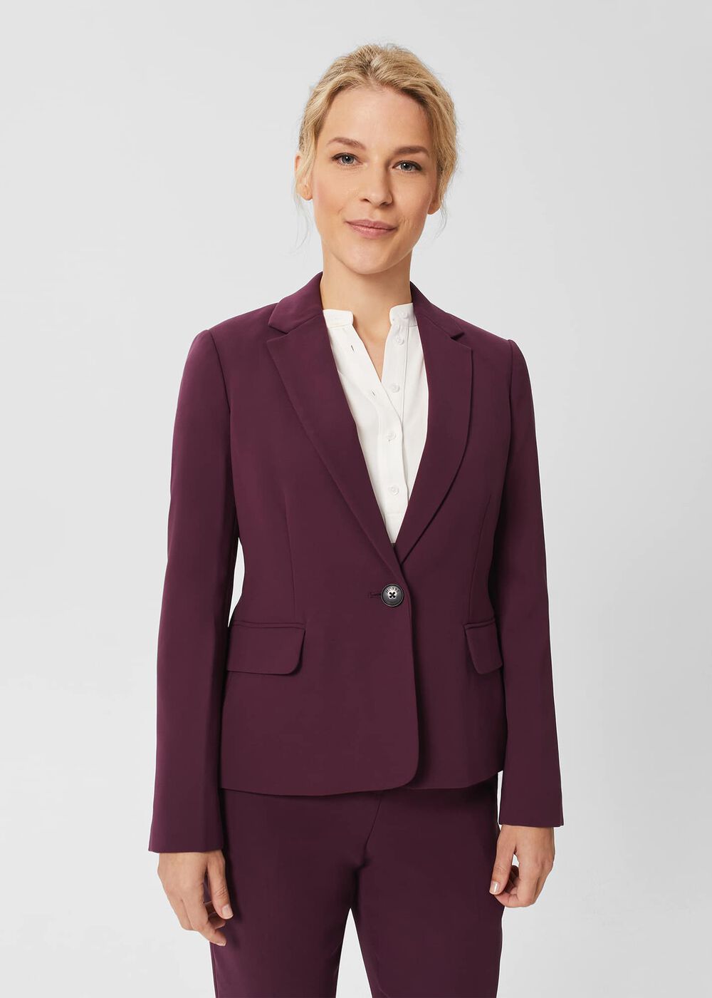 A woman wearing a deep purple tailored jacket with a notch lapel collar, front flap pockets, and a single button, paired with matching pants.
