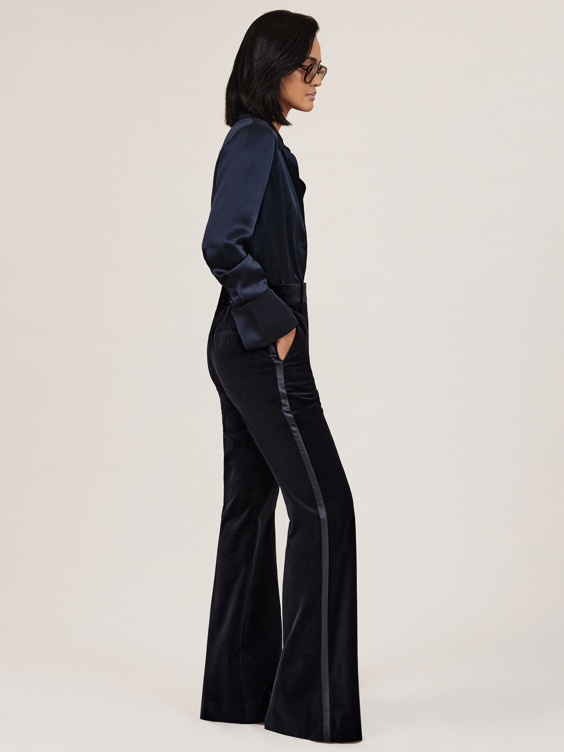 A woman wearing navy velvet satin-stripe flared trousers with side pockets and a matching navy satin blouse.