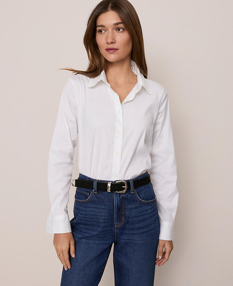 A woman wearing a white ruffle collar shirt with long sleeves, button front, and shirttail hem, paired with blue jeans.