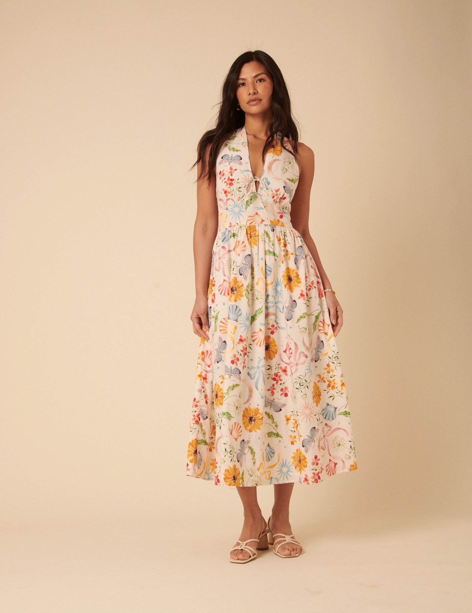A woman wearing a white floral midi dress with a halterneck, floral print, and side pockets.