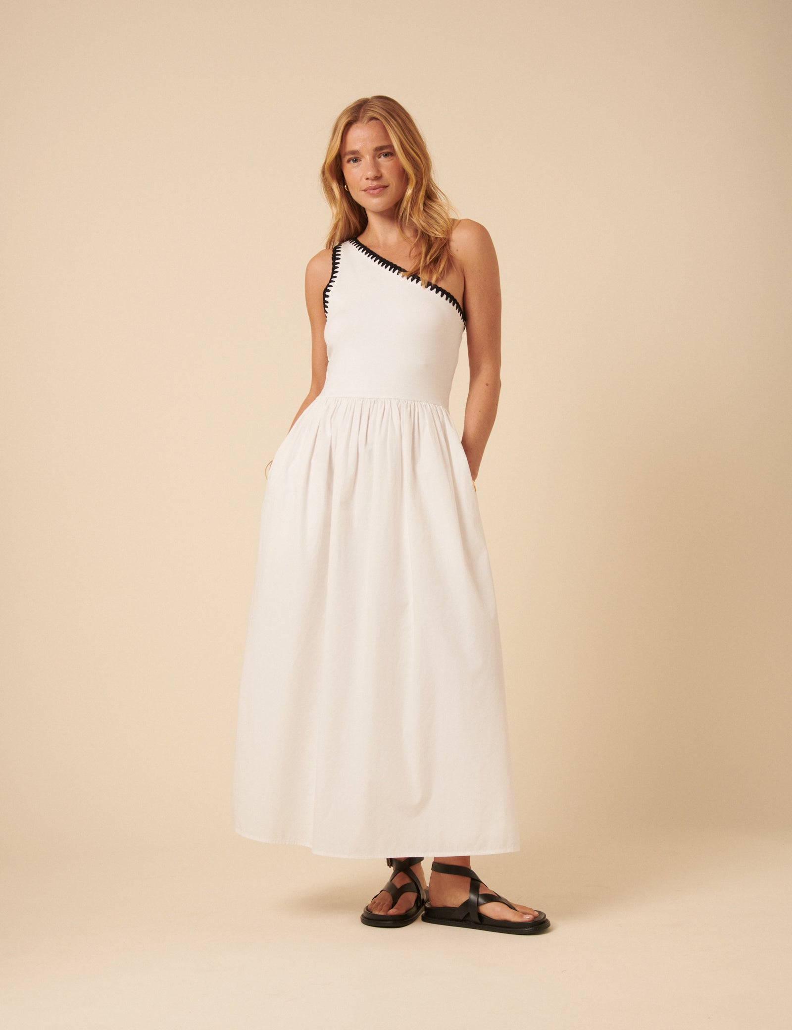 A woman wearing a white one-shoulder midi dress with crochet trim and a flowy skirt.