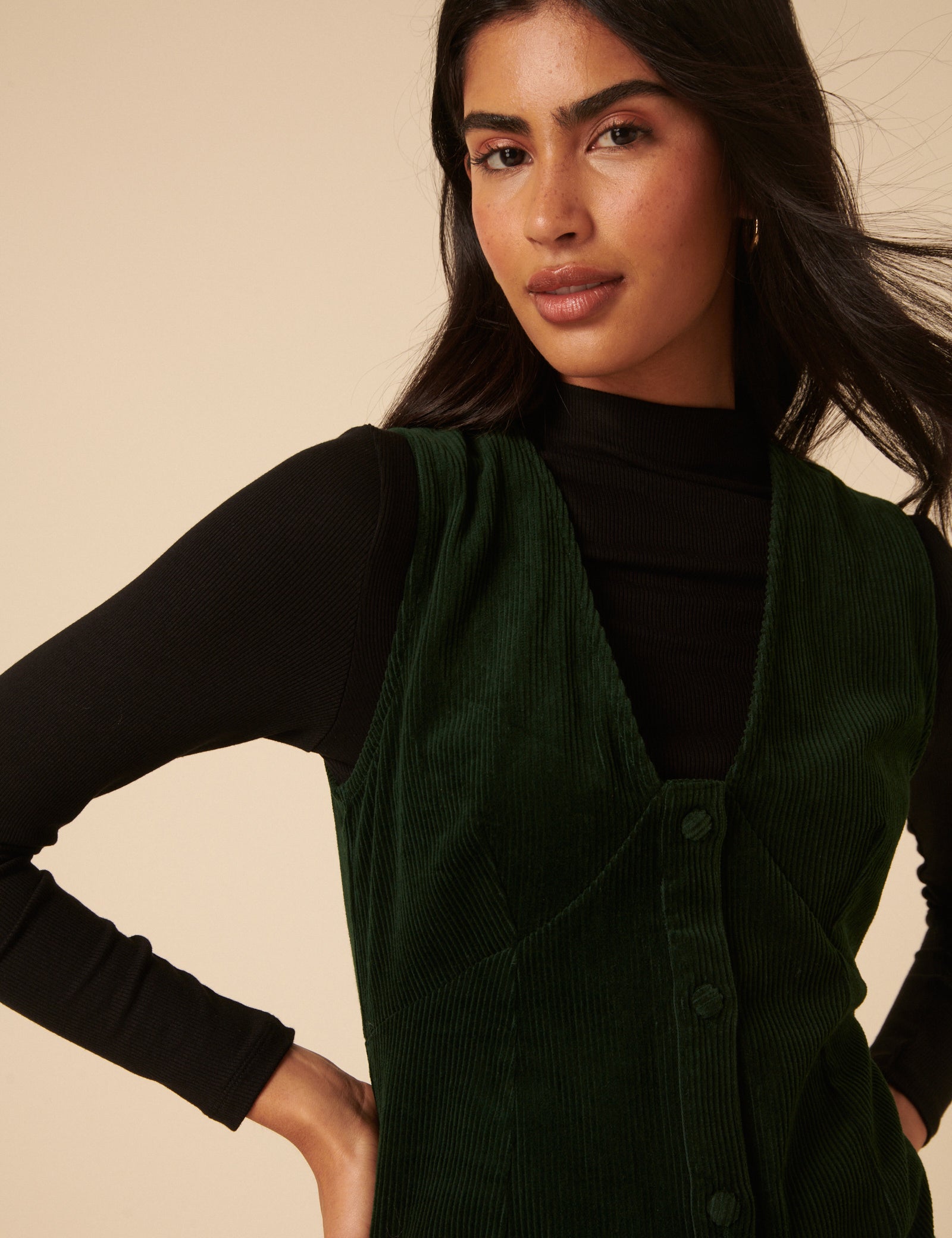 A woman wearing a khaki green cord mini dress with a scalloped V-neckline and button-front closure.