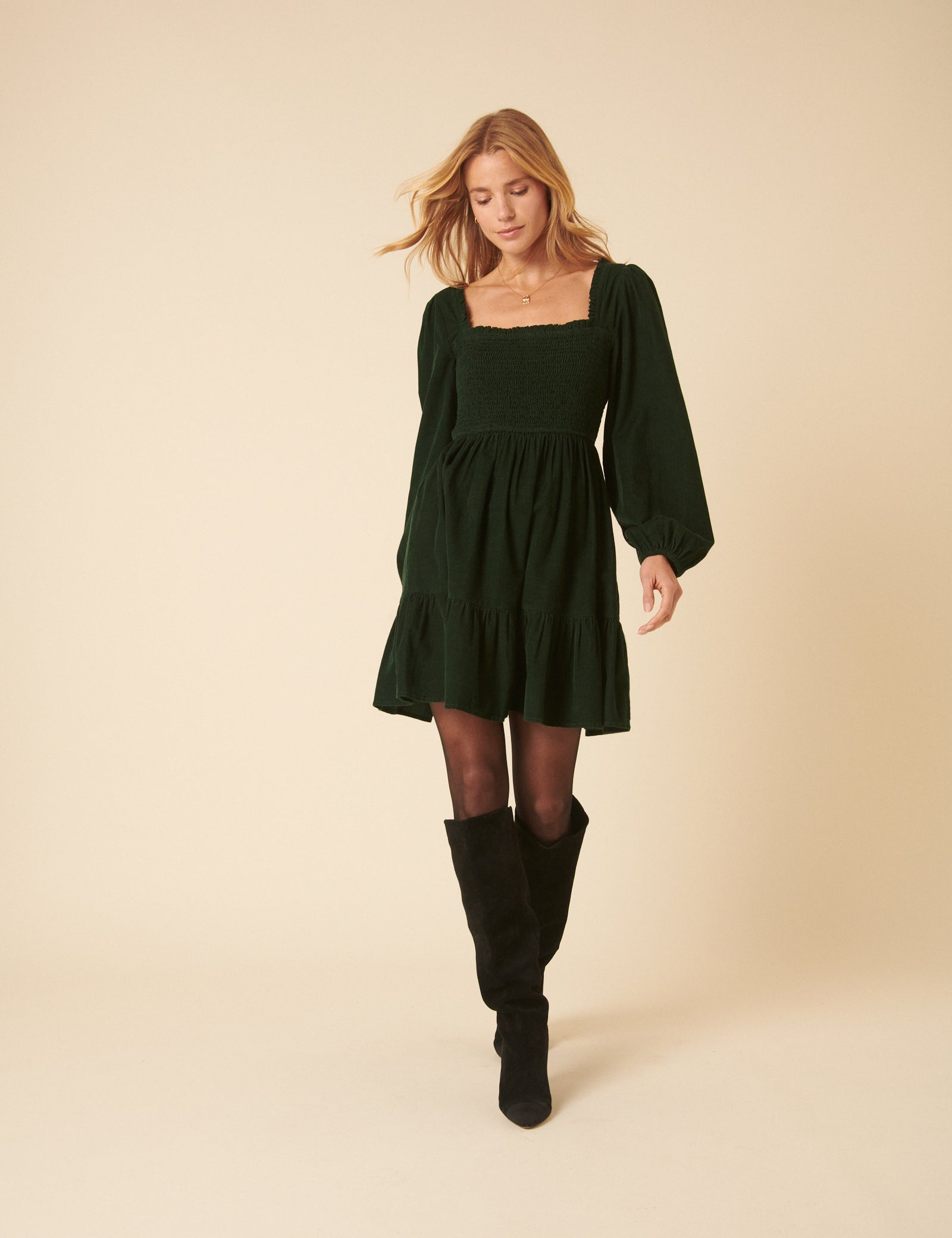 A woman wearing a dark green mini dress with long balloon sleeves, a square neckline, and a tiered hem.