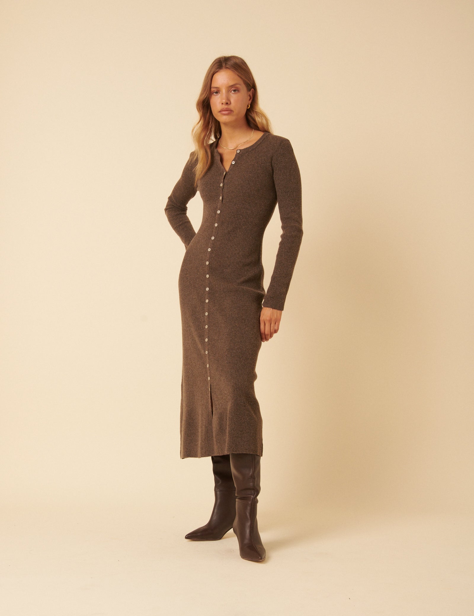 A woman wearing a brown ribbed knitted midi dress with long sleeves and a button front, standing against a plain background.