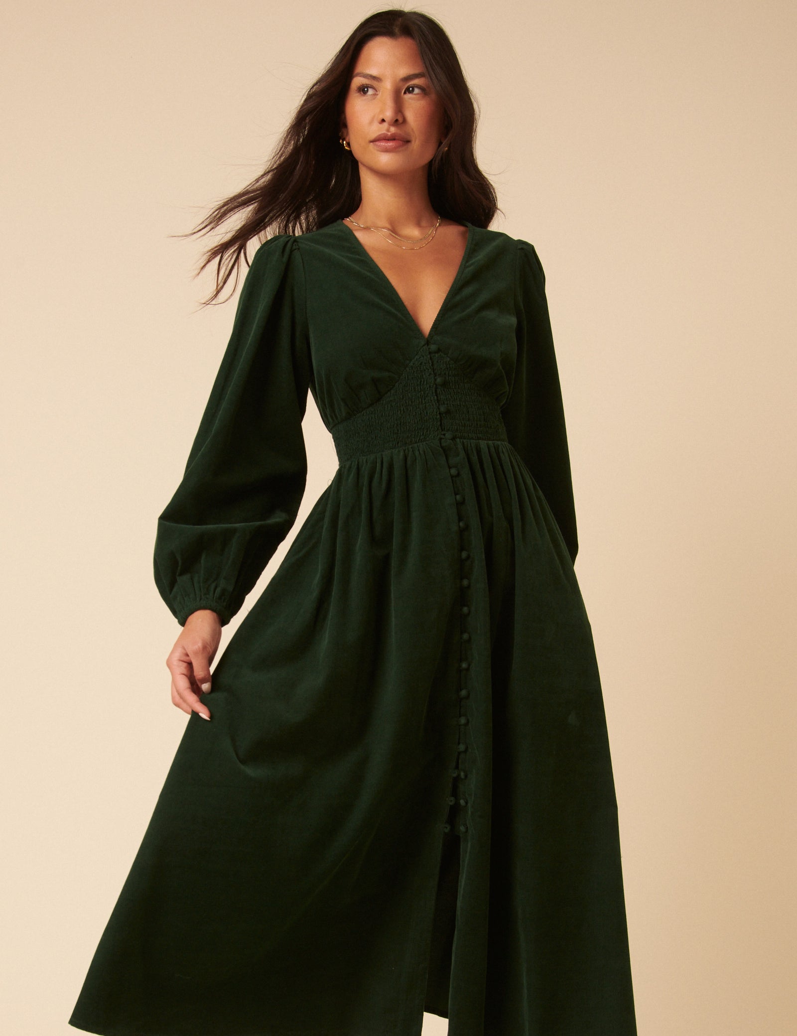 A woman wearing a forest green midi dress with long balloon sleeves, a V-neckline, and a full skirt.