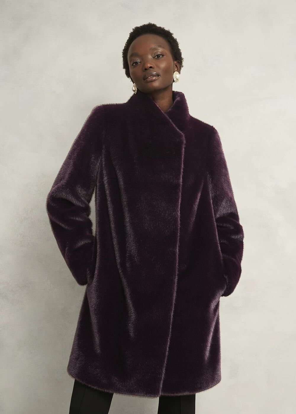 A woman wearing a deep purple faux fur coat with a longline fit, funnel neck, and side pockets.