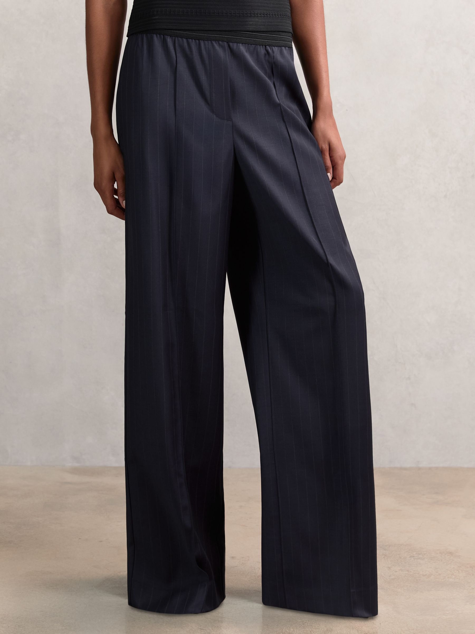 A pair of navy wide-leg trousers with pinstripes, elastic waistband, and front pintucks, shown on a person.