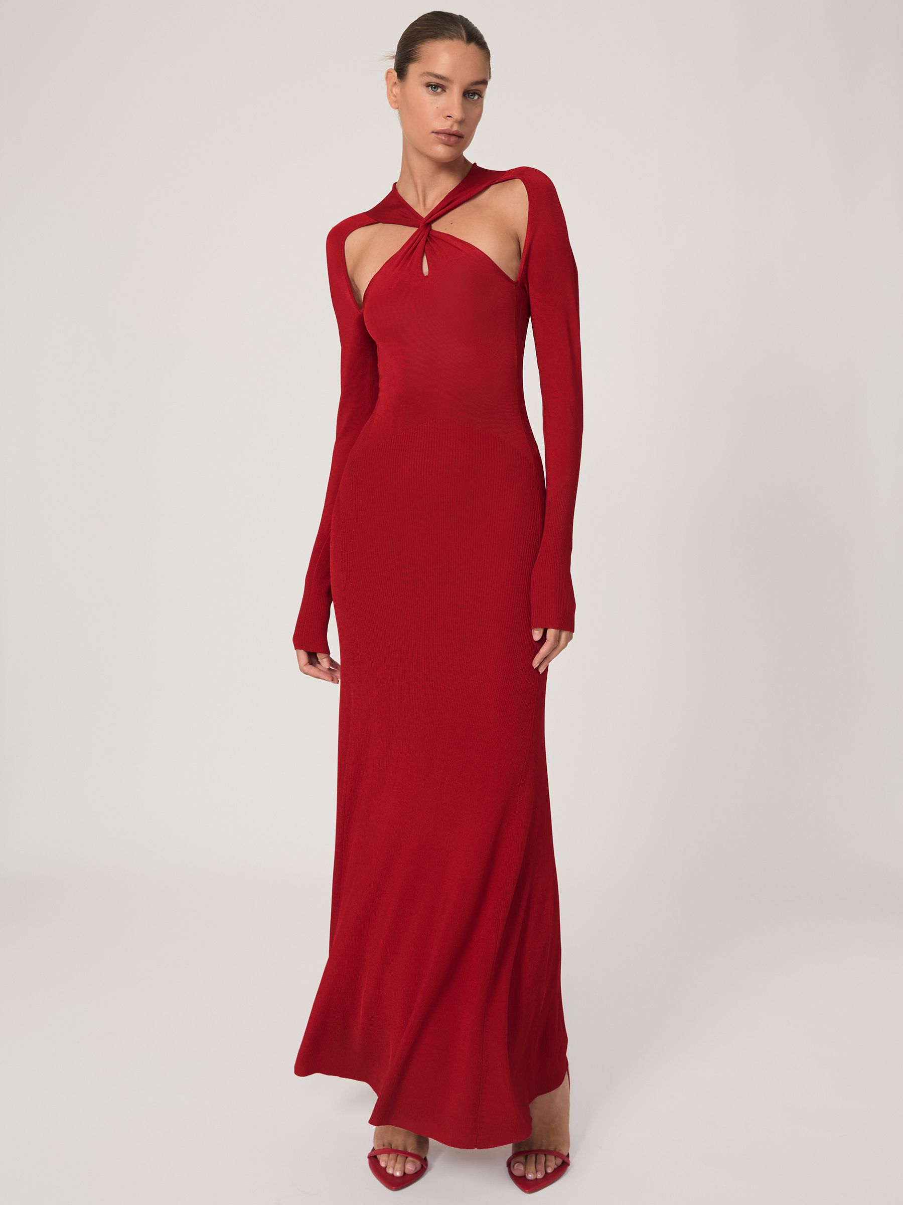 A woman wearing a red knitted maxi dress with cut-outs at the chest and back, long sleeves, and a high neckline.