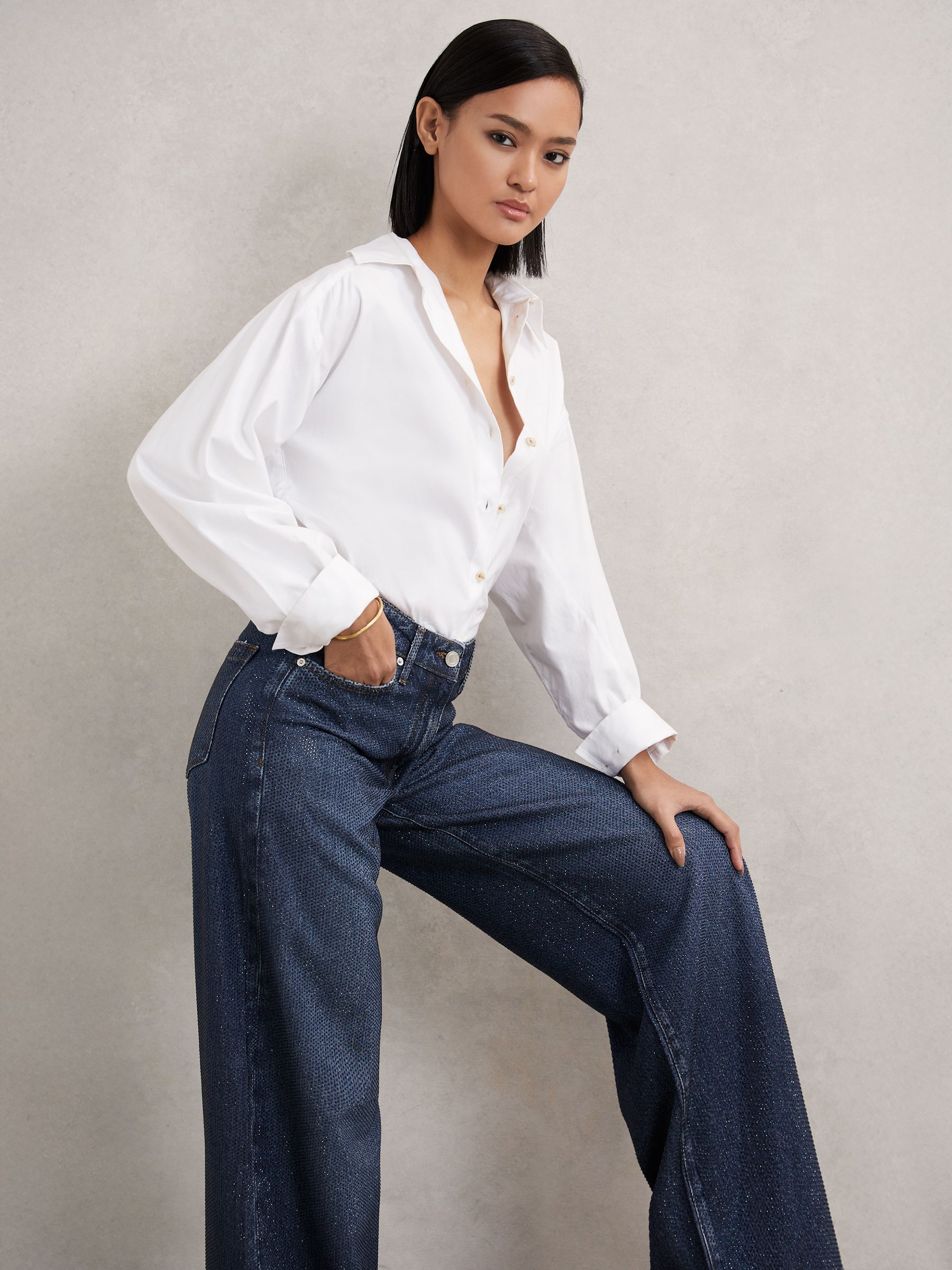 A pair of dark blue petite wide-leg jeans with crystal embellishments, shown with a white shirt.