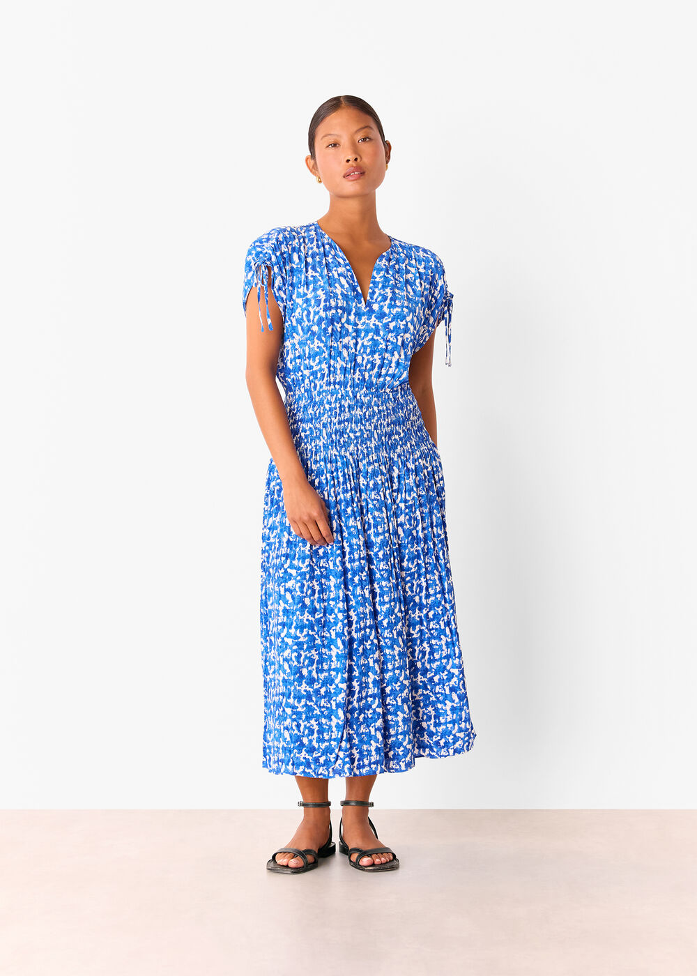 A woman wearing a blue and white brushed stroke midi dress with short sleeves, V-neckline, and a fitted waist.