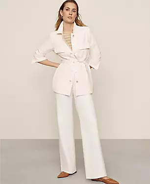A woman wearing white tailored trouser jeans with a high-rise waist, front zip, and belt loops, paired with a white jacket and beige shoes.