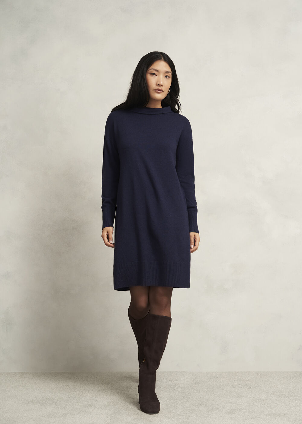 A woman wearing a navy blue knitted mini dress with a roll neck and long sleeves, paired with brown knee-high boots.