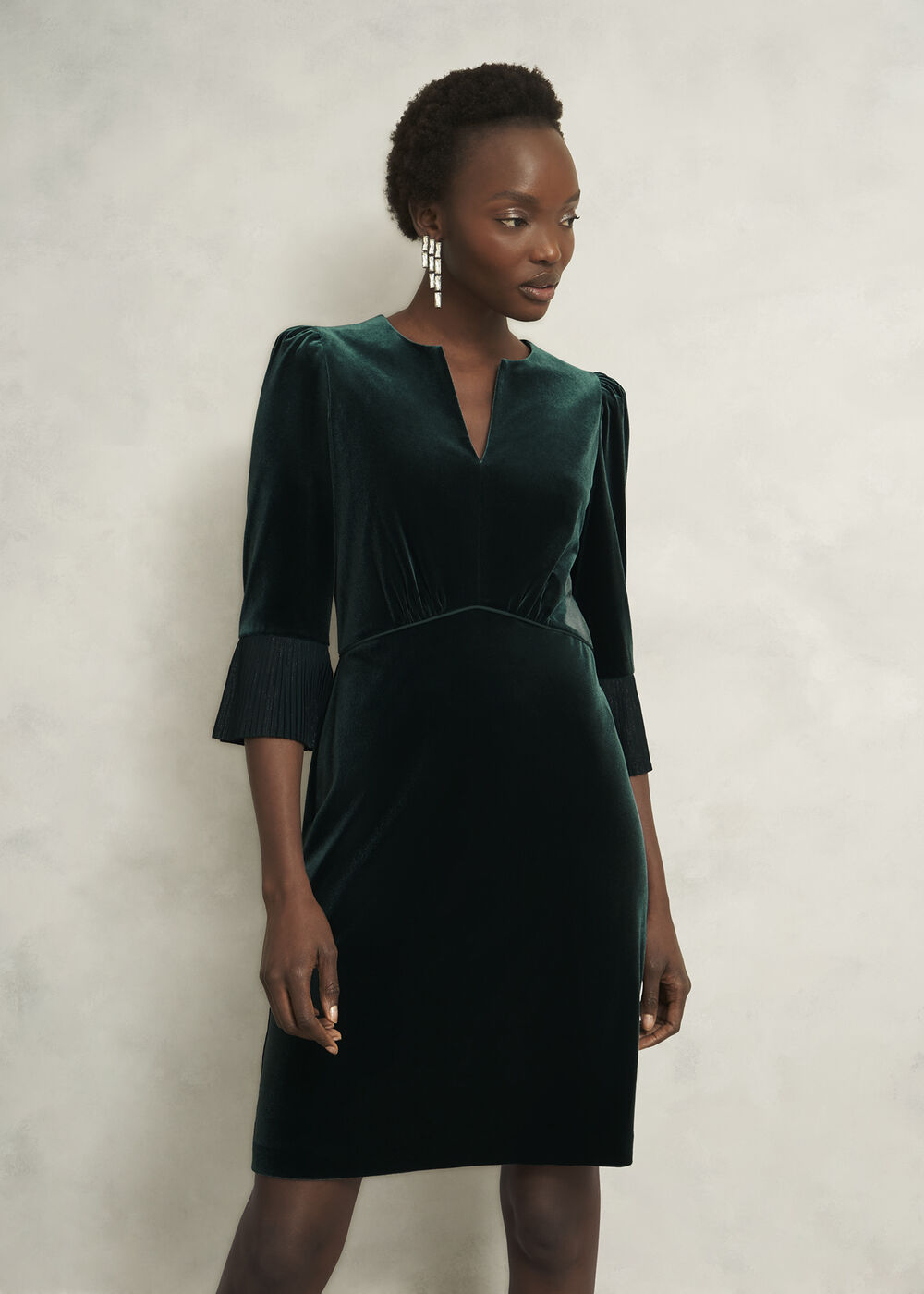 A woman wearing a deep violet velvet shirt dress with a button front, utility pockets, and a tie waist.